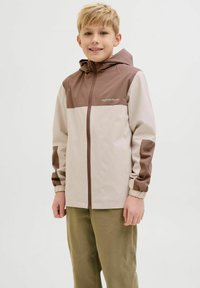Veste légère à capuche avec un design en blocs de couleurs beige et marron, dotée de poignets élastiques et d'une fermeture éclair sur le devant. Texture douce et lisse.