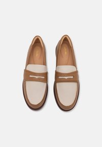 Leather loafers featuring a beige toe and brown vamp, with a decorative cutout and stitching details. Soft insole and rubber outsole.