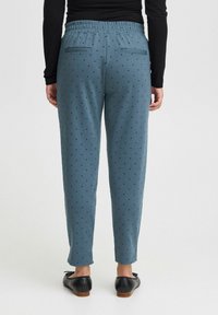 Blaue gemusterte Hose mit elastischem Bund, versehen mit kleinen schwarzen Punkten, zwei Gesäßtaschen und einem schmal zulaufenden Bein.