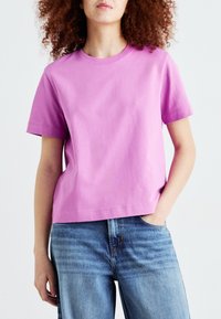 T-shirt a maniche corte, collo rotondo, in cotone rosa brillante, con una vestibilità comoda. Abbinato a jeans in denim blu chiaro.