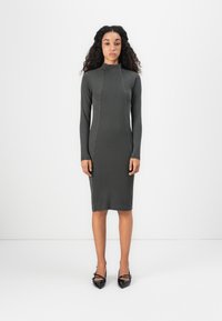 Dlhý rukáv, rebrované šaty v tmavošedej farbe s vysokým výstrihom a priliehavým strihom. Doplněné o čierne lodičky s špicatou špičkou na kontrast.