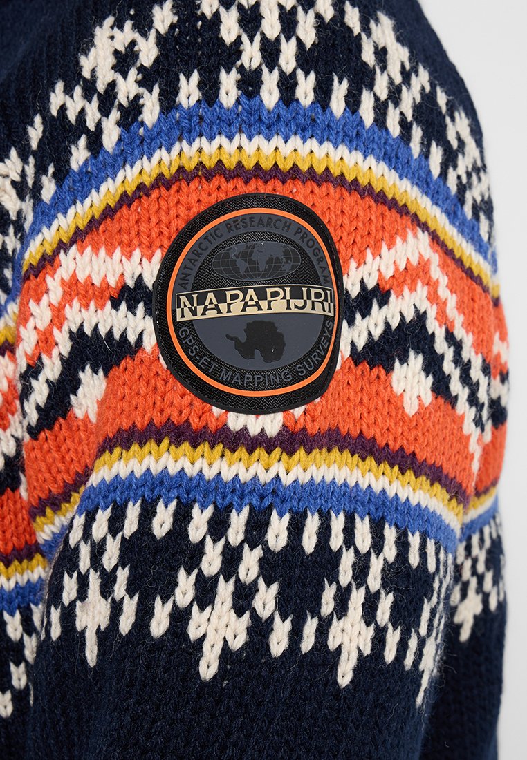 Pull en tricot présentant une base bleu marine avec un motif géométrique multicolore en blanc, orange, jaune et bleu. Comprend un patch logo noir.