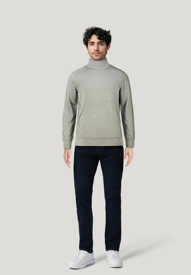 Suéter de cuello alto gris claro con mangas largas, que presenta una textura suave y sutiles acentos acanalados, combinado con jeans oscuros y zapatillas blancas.