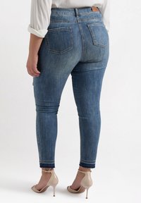 Skinny jeans in medium blue denim, featuring two back pockets and a frayed hem. Paired with nude, open-toe heeled sandals.
