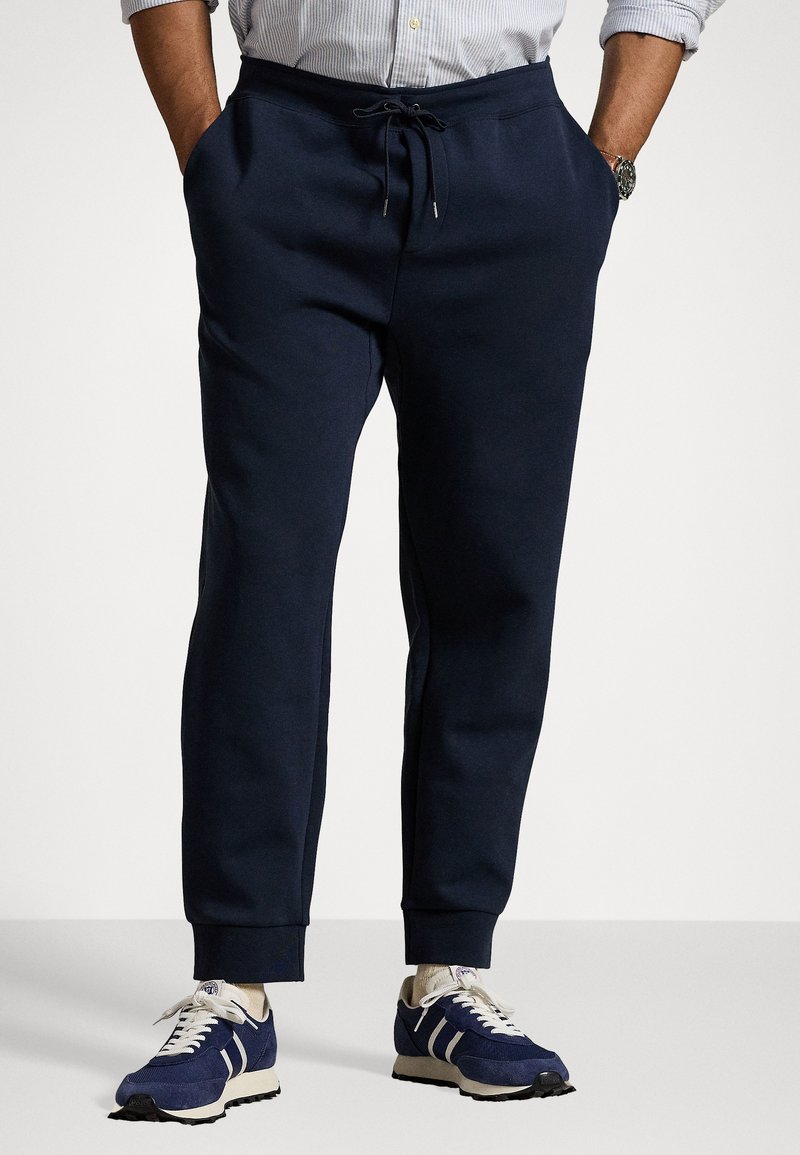 Navy blue sweatpants in soft material with an elastic waistband, drawstring, and side pockets. Paired with navy athletic sneakers.