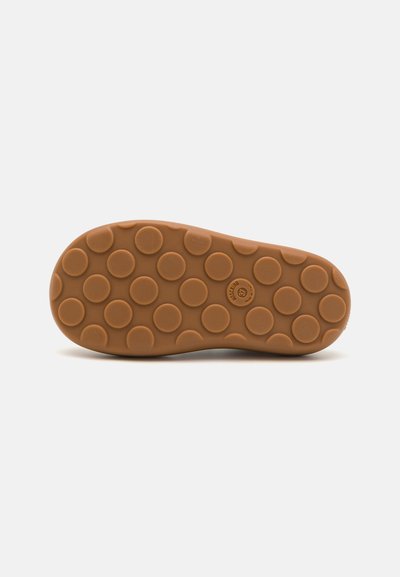 Semelle de chaussure en caoutchouc de couleur brun clair avec des motifs texturés circulaires. Caractéristiques de traction proéminentes et un logo légèrement surélevé au centre.