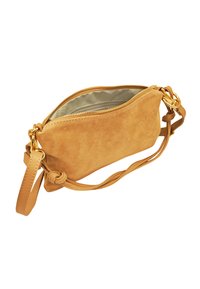 Pochette en suède beige avec fermeture éclair, bandoulière unique réglable et un accent noué sur la bandoulière. Intérieur doublé en tissu léger.