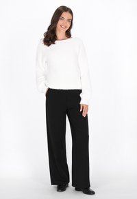 Pulover alb tricotat cu guler rotund, croială lejeră și mâneci lungi. Asortat cu pantaloni negri, cu croială largă și pantofi negri.