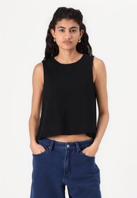 Svart ärmlös crop top i mjukt tyg med rund halsringning. Parat med högmidjade blå jeans med stora fickor.