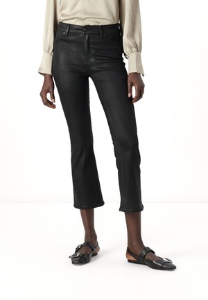 Black cropped jeans with a fitted design, made of smooth denim. Paired with flat black shoes featuring a buckle detail.