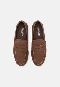 Bruna mockaläder loafers med kontrasterande sömmar, läderrem över vampen och en strukturerad innersula. Timberland-logotyp på innersulorna.