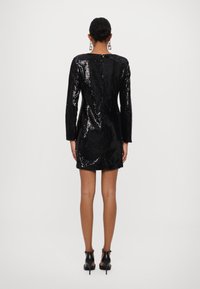 Abito nero di paillettes con maniche lunghe, scollatura rotonda e cerniera nascosta sul retro. Presenta una silhouette aderente con una texture liscia.