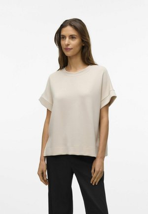 Beige short-sleeve top made of soft fabric, featuring a round neckline and a relaxed fit, paired with black trousers.