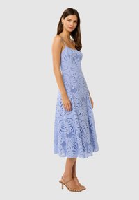 Abito in pizzo azzurro chiaro con corpetto aderente e gonna a trapezio. Presenta spalline sottili, modelli intagliati intricati e un orlo fluente.