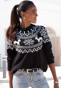 Schwarzer Strickpulli mit weißem Fair Isle-Muster, das Rentiere und Schneeflocken zeigt. Kombiniert mit hellblauen Jeans und einem schwarzen Gürtel.