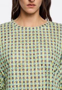 Multicolore top met een geruit patroon in groen, geel en bruin, met een ronde halslijn en een gestructureerde stof.