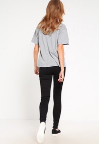 Graues kurzärmliges T-Shirt mit rohem Saum, kombiniert mit schwarzen engen Jeans und schwarzen Slip-On-Sneakers, von hinten betrachtet.