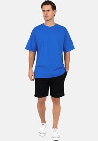 T-shirt en coton bleu à manches courtes, associé à un short noir et des baskets blanches, avec un design simple et une coupe décontractée.