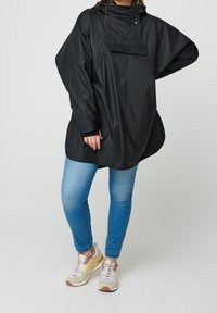 Sort vandtæt parka med hætte, der har trykknaplukning og oversized design. Matchet med lyseblå jeans og multicolore sneakers.