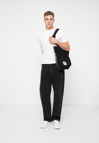 Svart kanvas tote-väska med dragkedja, bärs över axeln. Kombination med en enkel vit t-shirt och mörka jeans, vilket ger en avslappnad look.