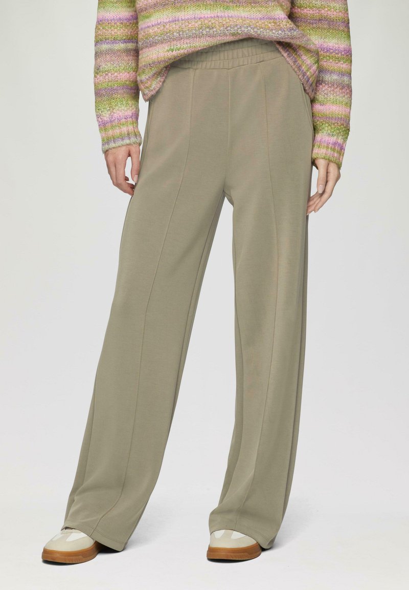 Khaki wijde broek met een soepele textuur en details van de voorkant, gecombineerd met witte en tan sneakers op een effen achtergrond.