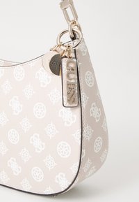 Rosa Handtasche aus Kunstleder mit weißem Logo-Muster, geschwungener Form, goldfarbenen Beschlägen und dekorativen Anhängern mit dem Markennamen.