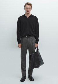 Maglione nero a maglia, pantaloni di lana grigi, cintura nera, borsa a tracolla nera in pelle, stivaletti neri lucidi, sfondo di colore uniforme.