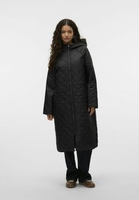 Abrigo largo acolchado negro con capucha, que presenta un cierre frontal de toda la longitud y mangas amplias. Textura suave, corte recto y diseño minimalista.