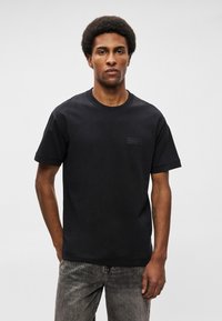 Μαύρη βαμβακερή μπλούζα T-shirt με κοντά μανίκια, στρογγυλή λαιμόκοψη και μικρή ορθογώνια ετικέτα λογότυπου στο στήθος. Λείο υλικό, άνετη εφαρμογή.