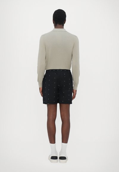 Helles graues Langarmoberteil kombiniert mit schwarzen Shorts, die ein dezentes Muster aufweisen. Weiße Socken und Schuhe runden das Outfit ab.