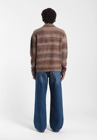Maglione a righe marroni realizzato in materiale morbido, abbinato a jeans di denim blu a gamba larga. L'outfit è mostrato da dietro.