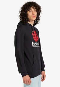 Sort hættejakke lavet af bomuld med en frontlomme, der har et rødt logo og hvid tekst. Designet inkluderer en justerbar hætte og lange ærmer.