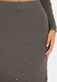 Jupe en tricot côtelé grise avec une silhouette ajustée, agrémentée de détails métalliques dispersés. Texture douce et design mi-long.