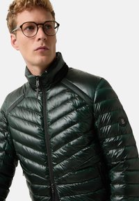 Zelená péřová bunda s lesklým povrchem, s horizontálním prošíváním, vysokým límcem a zipovým zapínáním. Obsahuje nášivku s logem na rukávu.