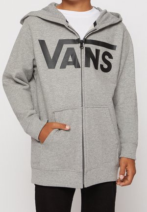 Enfant portant un sweat à capuche gris zippé avec le logo "VANS" en noir, des poches avant et une capuche, assorti à un pantalon noir.