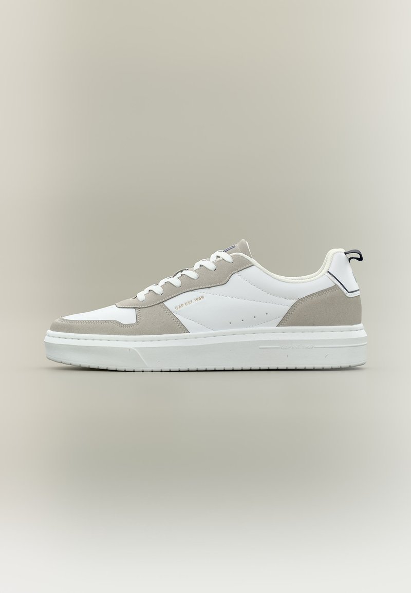 Λευκό χαμηλό αθλητικό παπούτσι με ανοιχτό γκρι επενδύσεις από σουέντ, λευκά κορδόνια, παχύ πάτο και κείμενο "GAP EST 1969" στην πλαϊνή πλευρά.