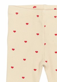 Beige leggings bordázott textúrával, kis piros szívmintákkal díszítve az anyagon. Puha és rugalmas anyag.