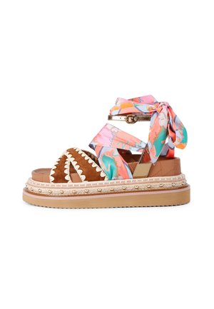 Sandalia de plataforma marrón con costuras crema, envoltura de seda en tonos pastel coloridos alrededor del tobillo y borde con tachuelas doradas en la suela.