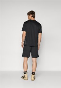 Chemise noire à manches courtes et short assorti, en tissu léger. Détails notables : coutures contrastées et chaussures d'escalade beiges avec accents noirs.
