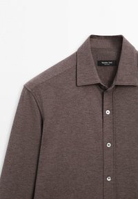 Brun langærmet skjorte med knapper og krave, synlige øverste tre knapper samt mærket "Massimo Dutti" indeni kraven.
