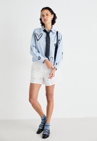 Blå och vit randig skjorta med knappar och svarta hjärt-mönster, kombinerad med vita shorts med scalloped nederkant och ögondetaljer.