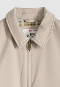 Μπεζ μπουφάν με γιακά και φερμουάρ μπροστά, με επένδυση από ύφασμα καρό ορατή μέσα στον γιακά, με φερμουάρ με σήμανση Levi's.