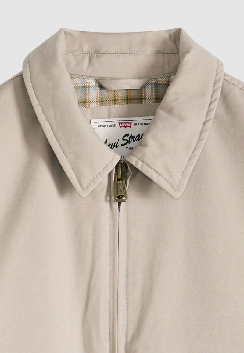 Giacca beige con colletto, chiusura frontale con zip e fodera interna a quadri visibile all'interno del colletto, dotata di cursore della zip marchiato Levi's.
