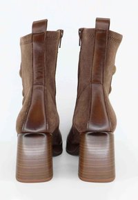 Stivali alla caviglia in suede marrone con tacco quadrato, chiusura con cerniera e bottoni decorativi sul lato. Materiale testurizzato e accenti lisci.