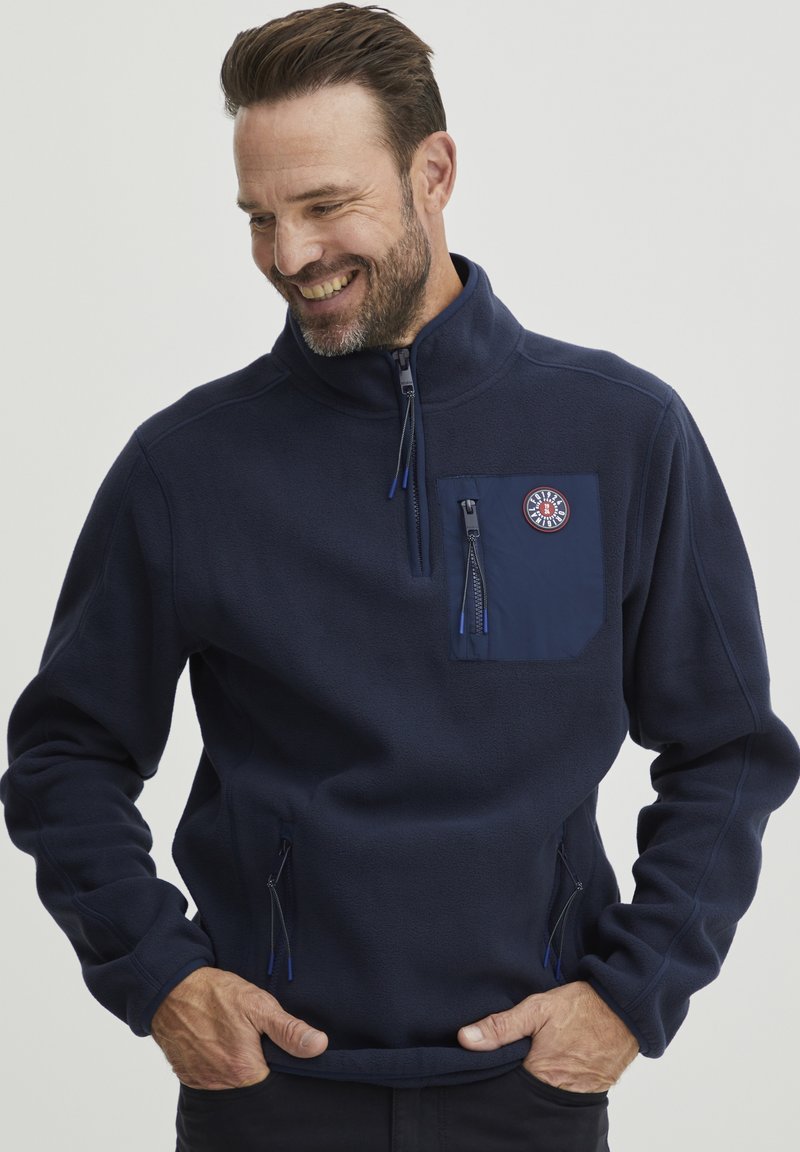 Marineblaue Fleece-Pullover mit halbseitigem Reißverschluss, Brusttasche und seitlichen Reißverschlusstaschen. Ausgestattet mit einem strukturierten Stoff und Logo-Detail auf der Brust.