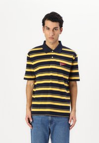 Marineblå og gulstribet polo-shirt med krave, korte ærmer og en lille rød mærke på venstre side.