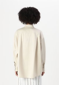 Beige langermet skjorte med avslappet passform, knappmansjett og en subtil glans. Designet med klassisk krage og rett bak.