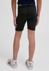 Svarta träningsshorts med en åtsittande design, elastisk midja med en logotyp, slät textur och enfärgad, kombinerade med lätta sneakers.