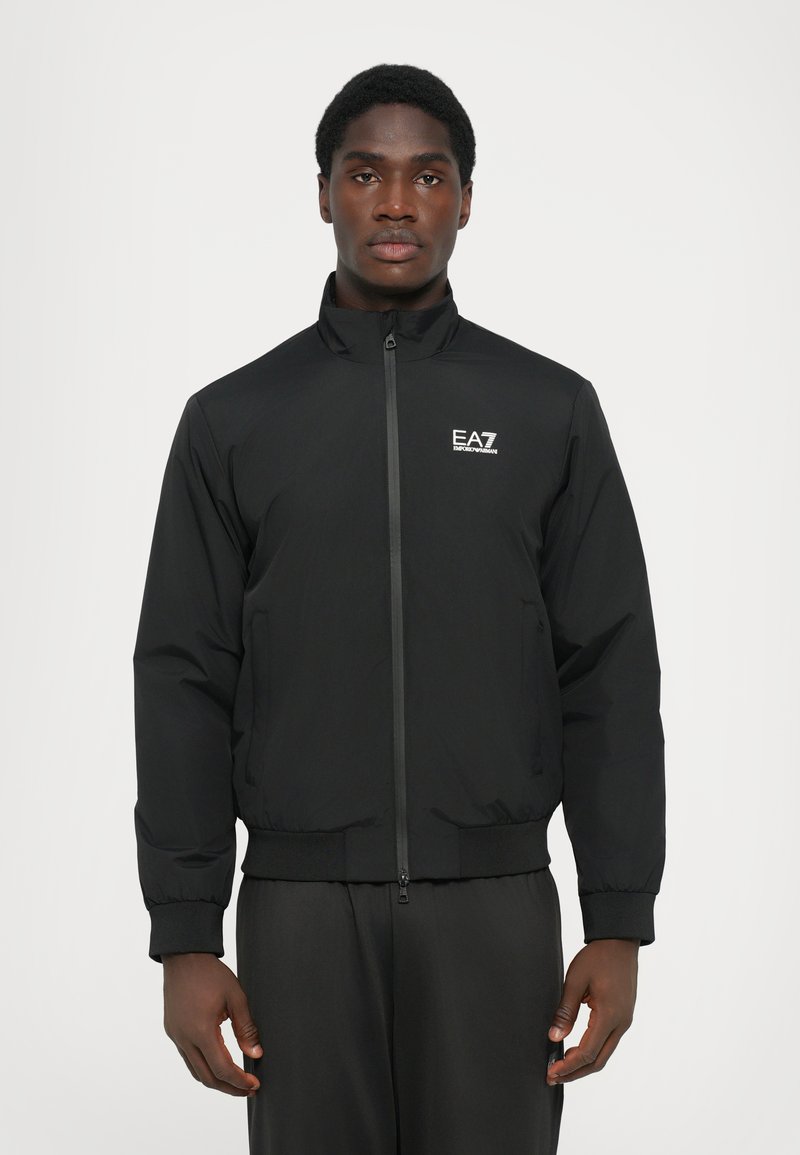 Black bomber jacket featuring a zip front, high collar, elastic cuffs, and hem. Includes a small EA7 logo on the left chest. Smooth texture.