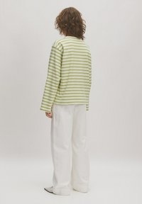 Gestreiftes langärmliges Oberteil in Hellgrün und Weiß, kombiniert mit lockeren weißen Hosen. Weicher Stoff mit lässiger Passform und minimalistischem Design.